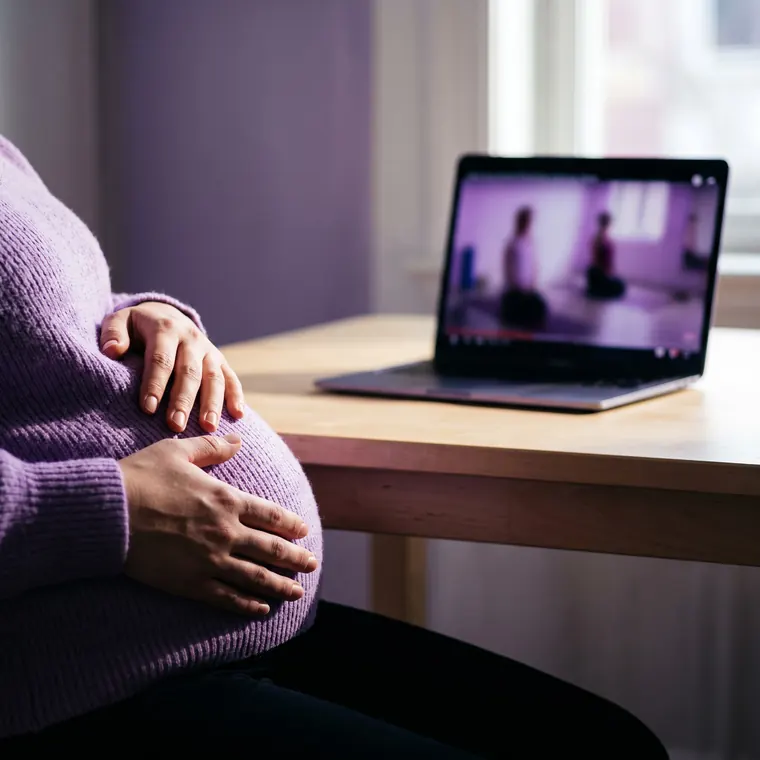 Gestante com a mão na barriga assistindo a uma aula no computador
